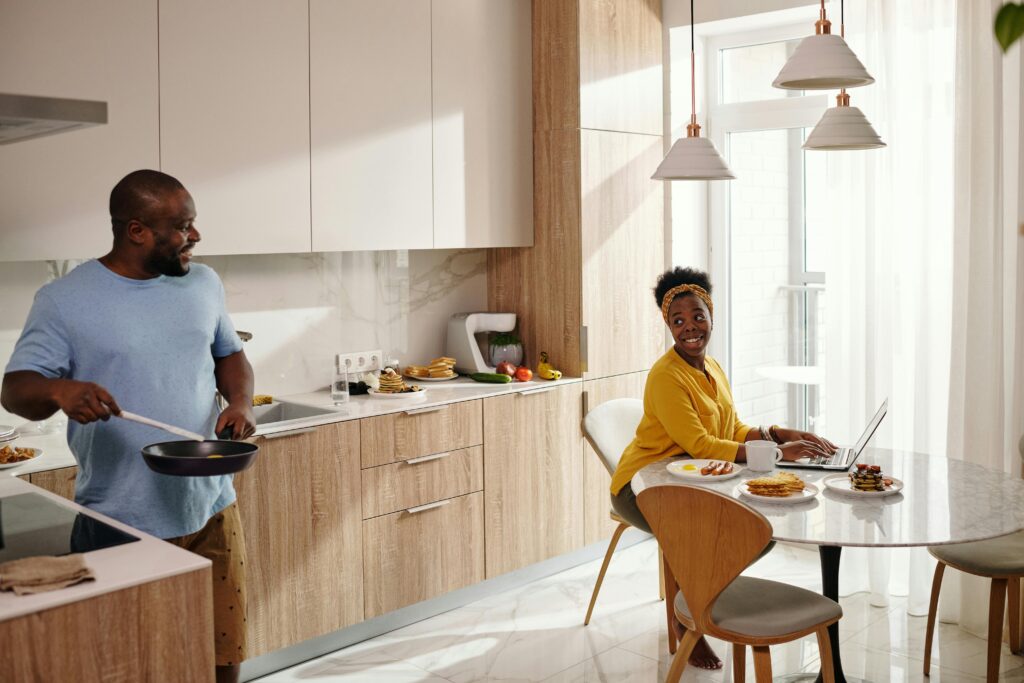 A couple enjoys their morning routine in a bright, modern kitchen, cooking and smiling.